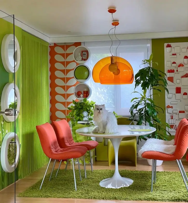 A 70s-style dining area with a white tulip table, orange chairs, a large orange dome light, and green shag rug.