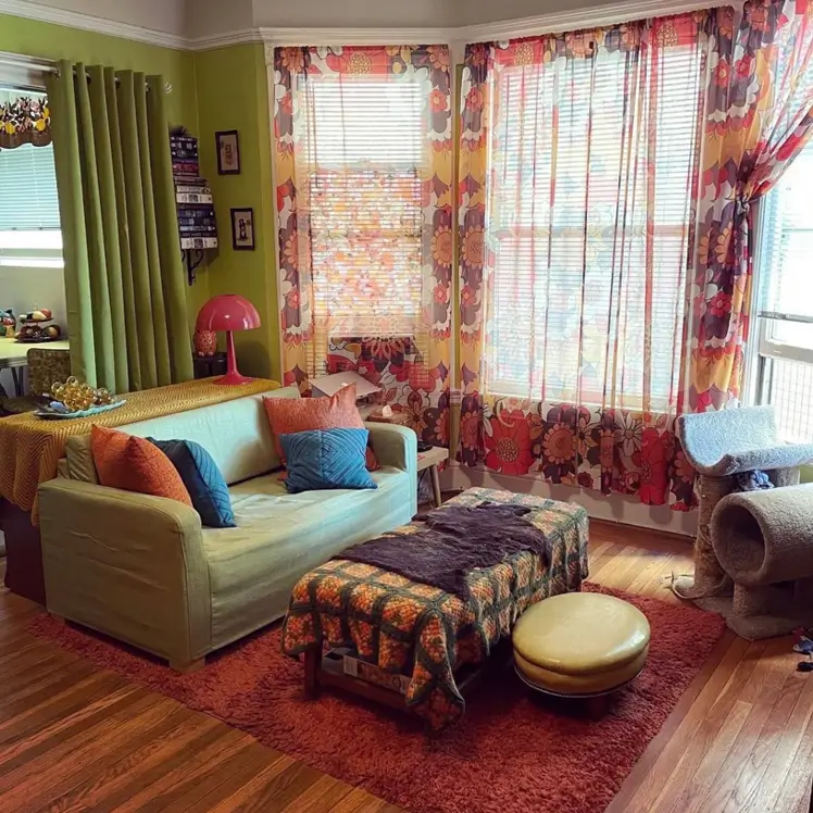 A 70s living room with large floral print curtains, a green sofa, and a rust-colored rug.