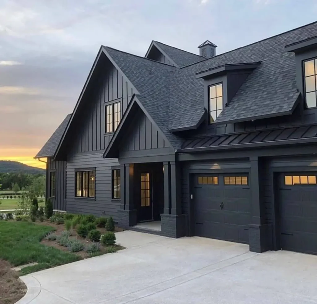 A modern black farmhouse exterior with prominent dormer windows and an attached garage at sunset.