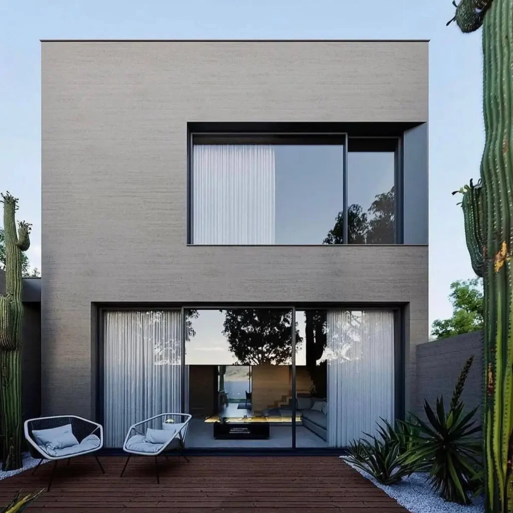 Modern minimalist gray house with large windows and a wooden deck featuring cacti and outdoor seating.