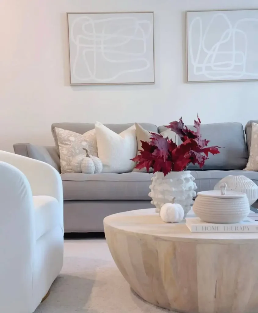 A neutral living room with a gray sofa, a light wood coffee table, and abstract art on the wall above.