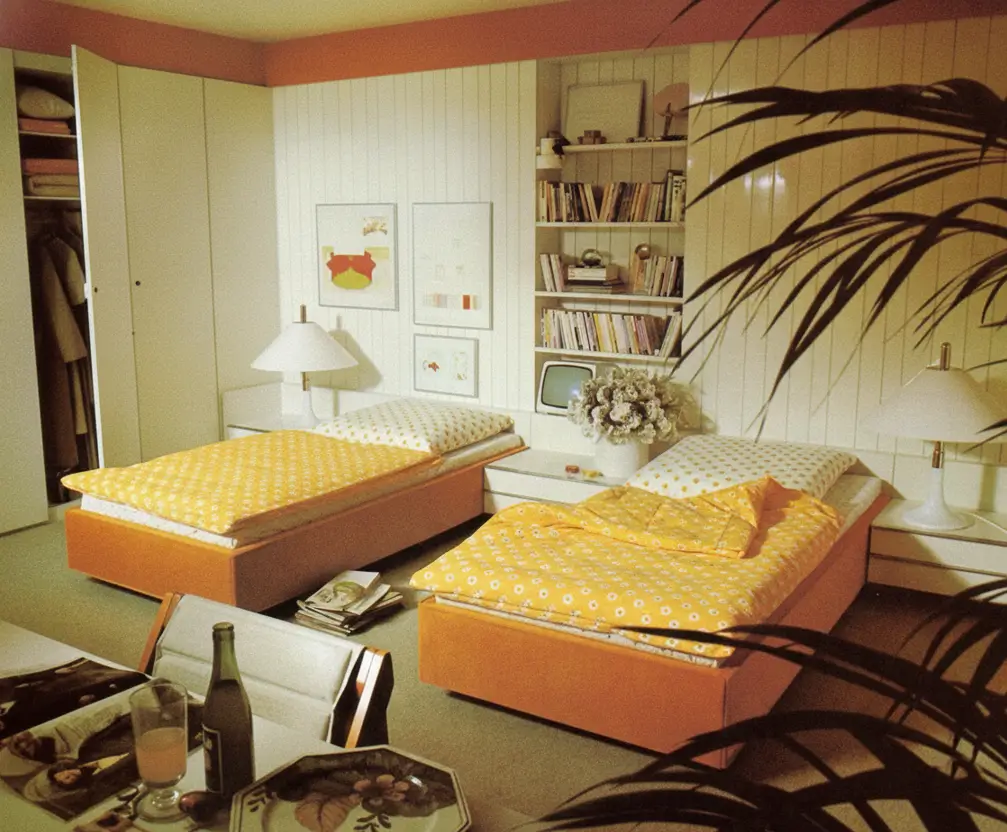 A functional 70s bedroom with twin beds, yellow bedding, and white modular shelving units.