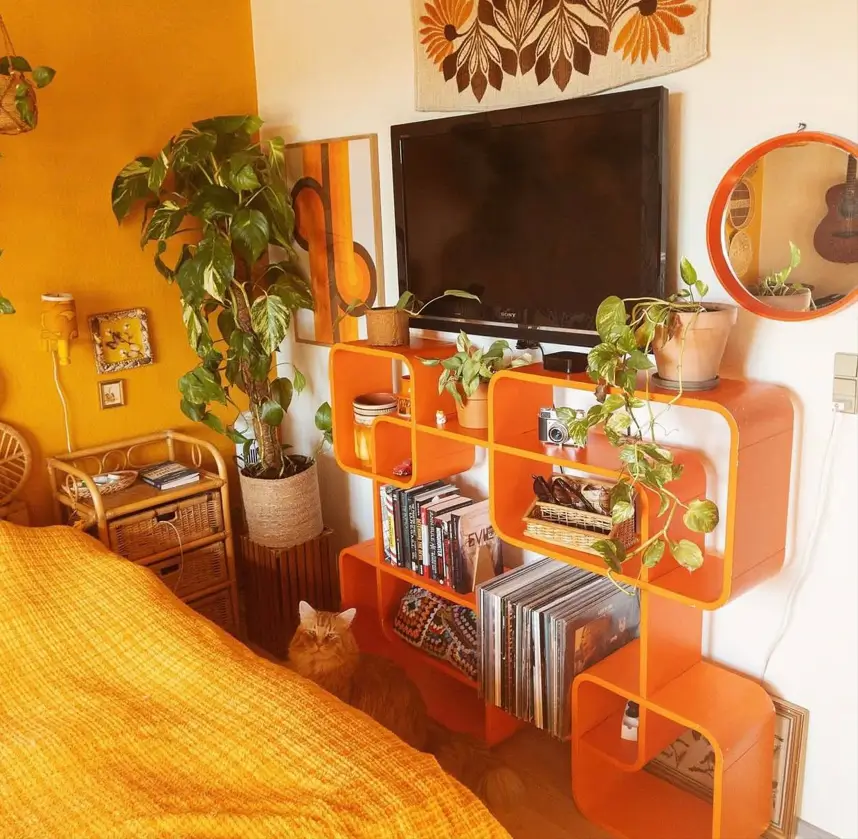 A bedroom with 70s interior design, featuring an orange modular shelving unit, a yellow bed, and a floral tapestry.