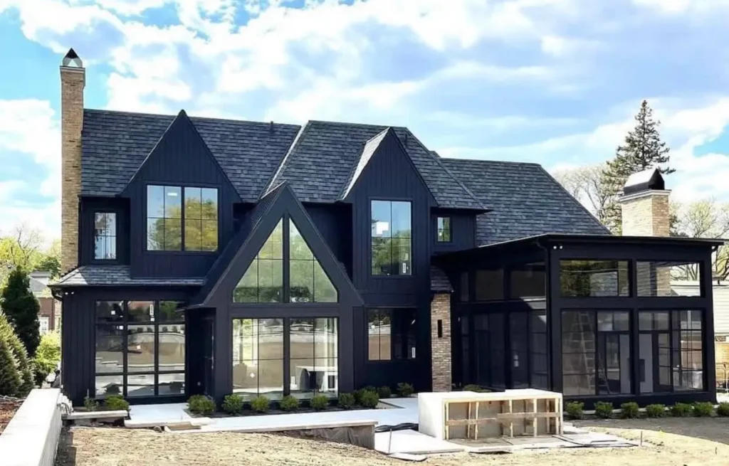A modern black farmhouse featuring extensive walls of glass for an indoor-outdoor feel and prominent brick chimneys.