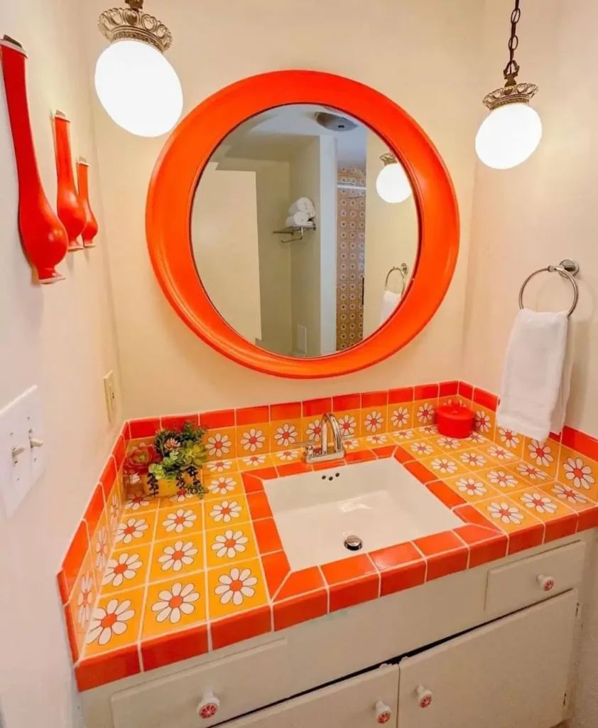 A retro 70s bathroom vanity with orange and yellow daisy-print "flower power" tile and a matching orange circular mirror.