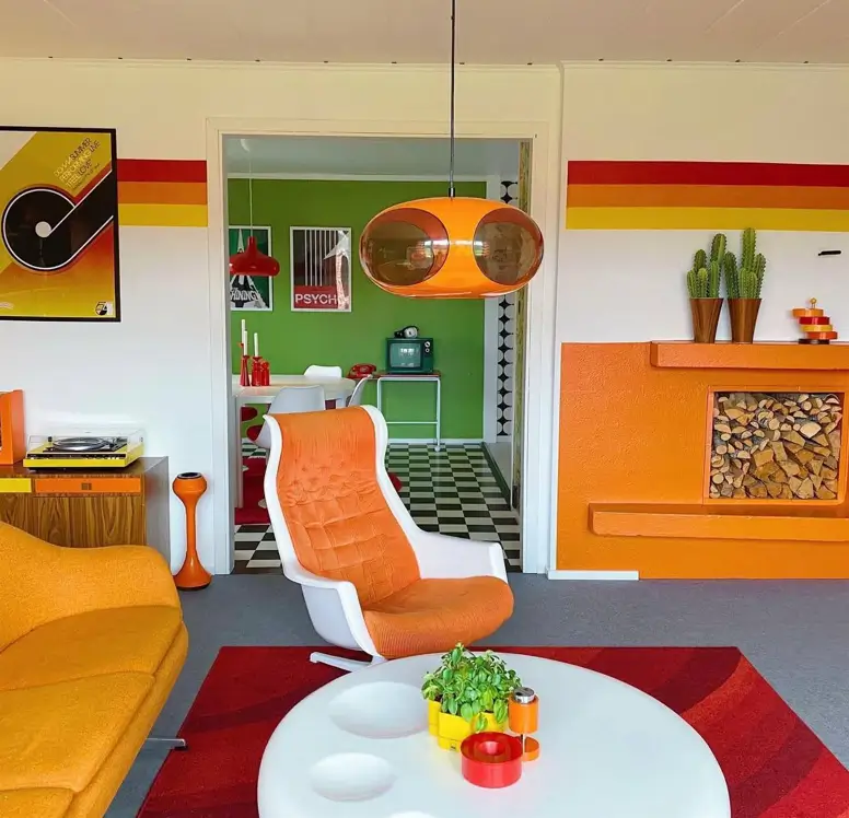 A living room with 70s interior decor, featuring bold orange and red wall stripes and a futuristic white and orange chair.