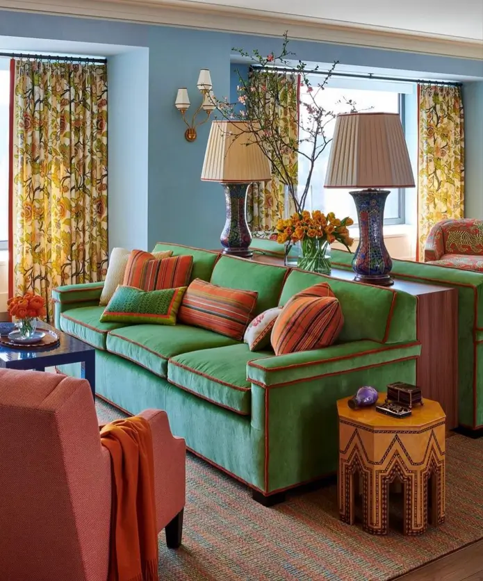 A 70s living room decor idea with a green velvet sofa, patterned curtains, and orange accents.