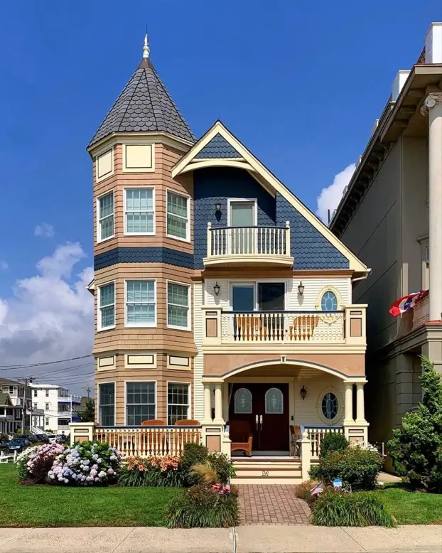 Colorful modern Victorian style home with a corner turret, blue and tan siding, and white balcony railings.