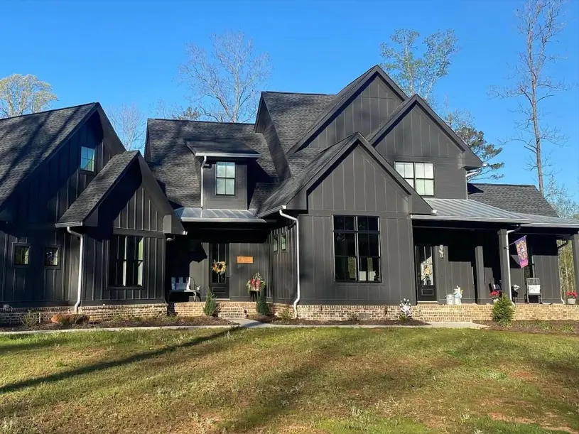 A modern black farmhouse with a light-colored brick foundation skirt that contrasts with the dark vertical siding.