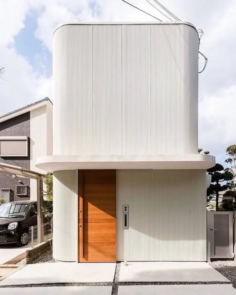 A modern Japanese house exterior in Osaka by SAI Studio, featuring a curved white facade and wood door.