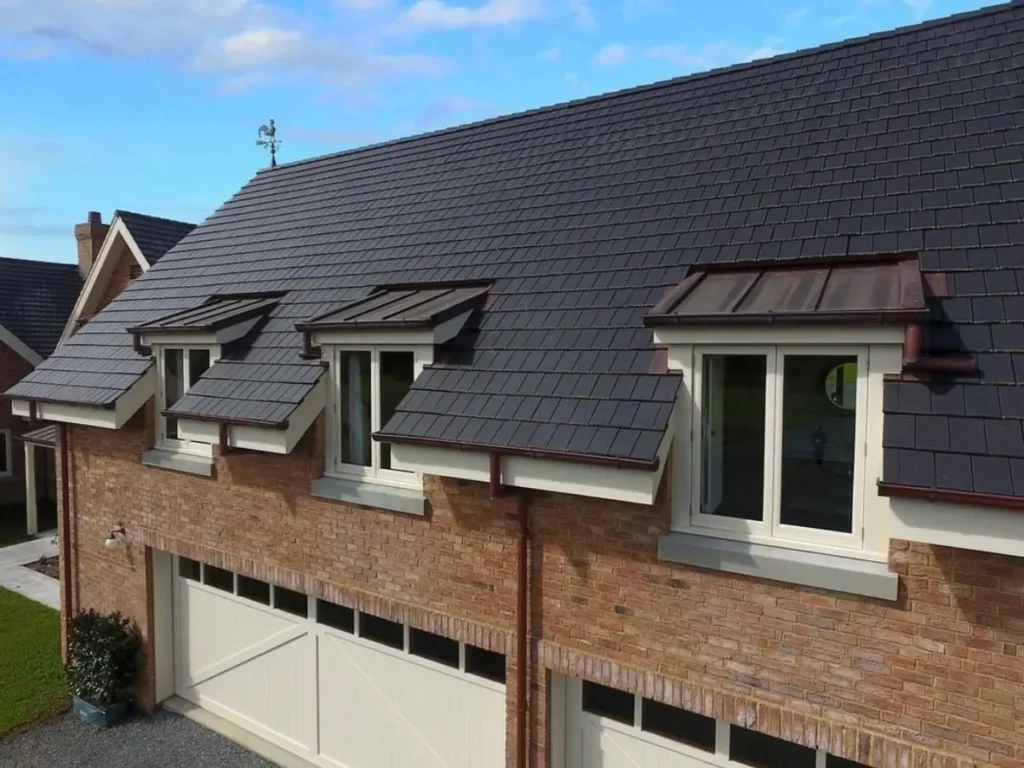 A modern brick home featuring three shed dormer windows with dark metal roofs and cream-colored trim.