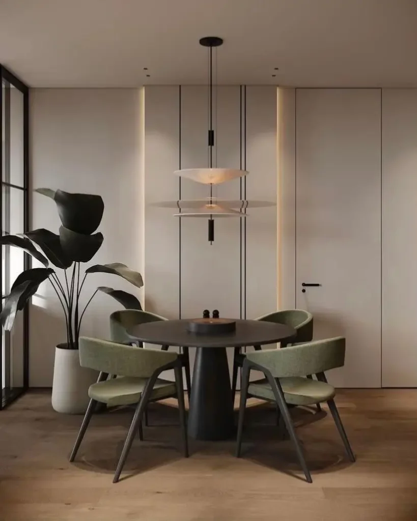 A modern condo dining room featuring a round black pedestal table and sage green upholstered chairs under a contemporary pendant light.