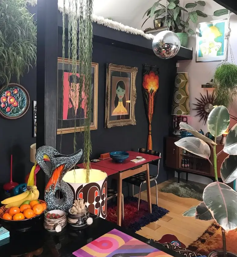 A moody room with 70s interior decor, featuring dark walls, a disco ball, a red dining table, and eclectic art.