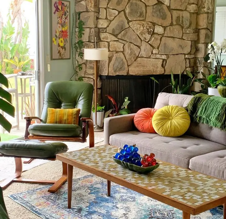 A 70s living room with a stone fireplace, a green leather lounge chair, and a mosaic tile table.