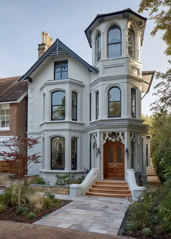 A modern Victorian style home in pale gray with an ornate turret and black window frames.