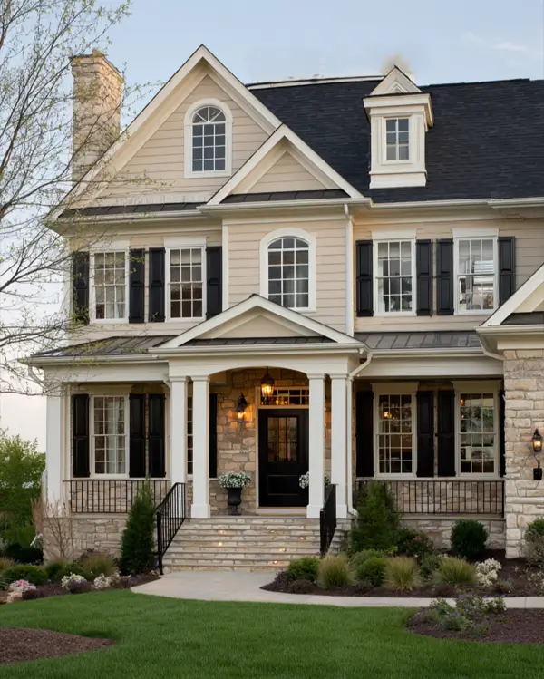 A traditional beige house with a stone foundation, black shutters, and white columns on the porch.