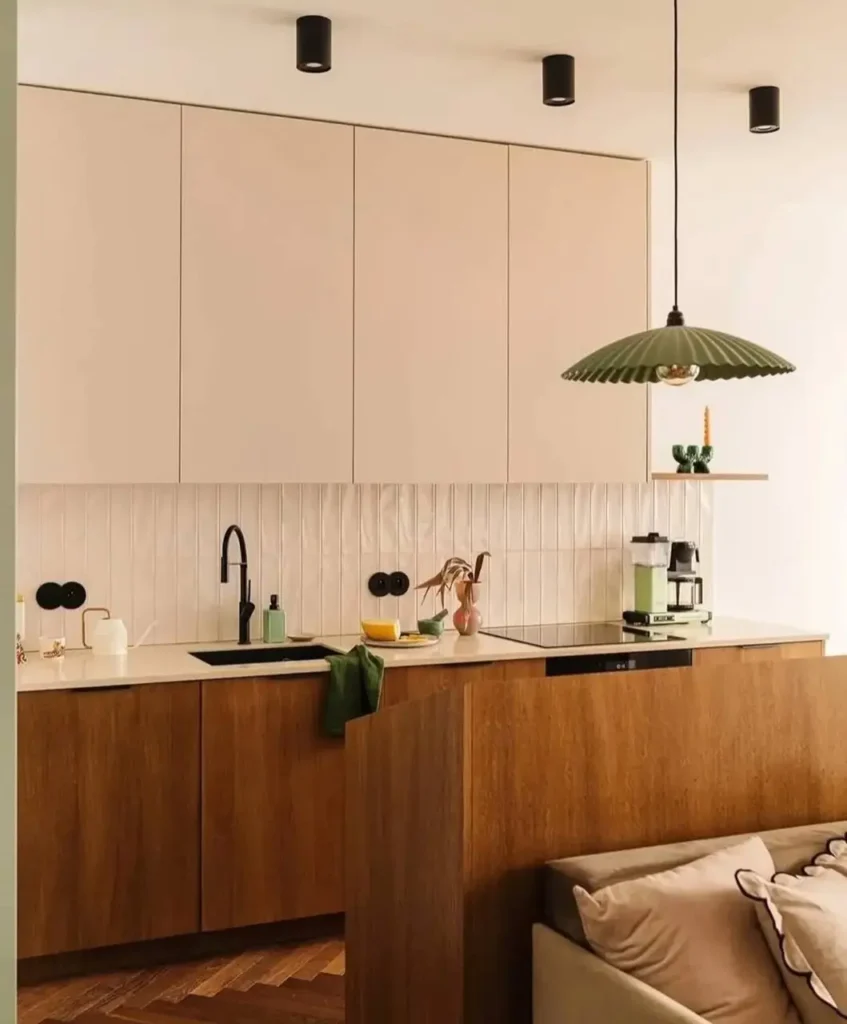 Modern minimalist kitchen with cream and wood two-tone cabinets, a black faucet, and a green pendant light.