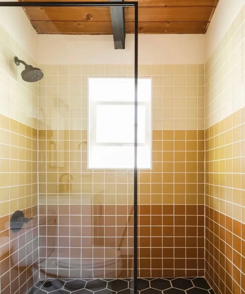 A modern 70s bathroom shower stall with horizontal striped tile in earth tones of cream, gold, and brown.