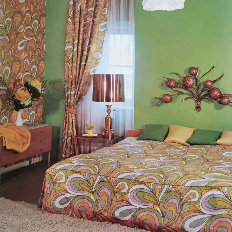 A retro 70s bedroom with matching psychedelic paisley print on the bedspread and curtains against a green wall.