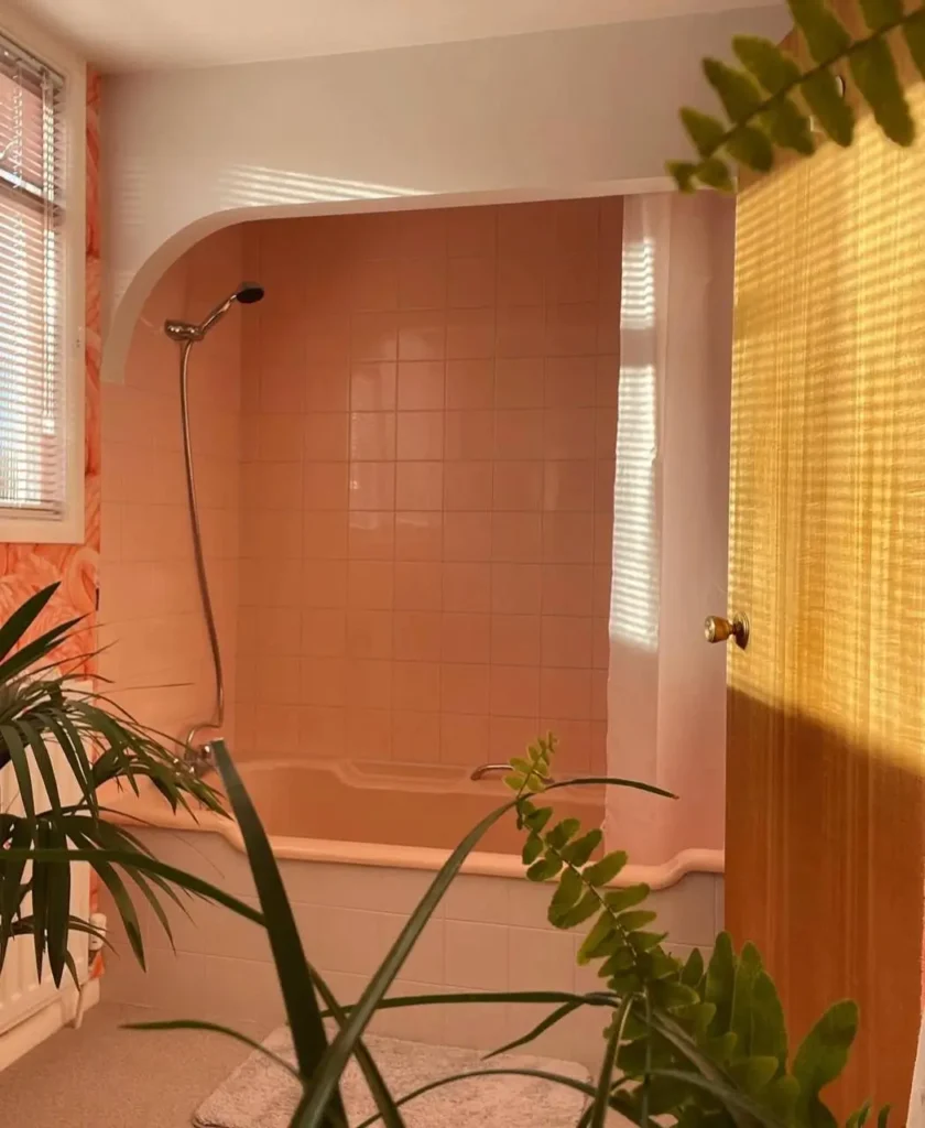 A 70s bathroom with a peach-colored bathtub and matching peach tile in a soft, arched alcove.