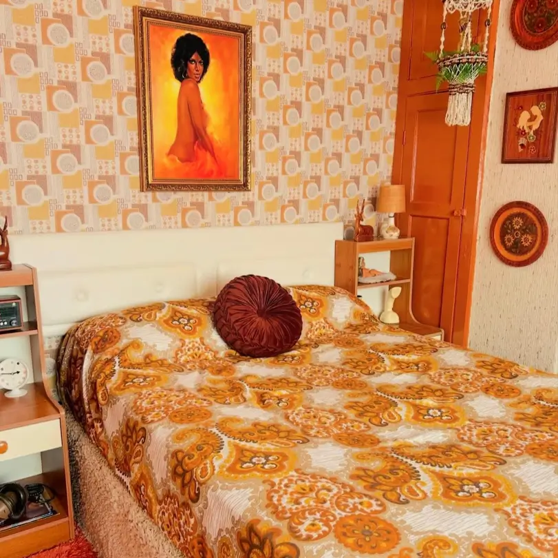 A 70s bedroom decor with geometric wallpaper and a matching paisley floral bedspread in warm tones.