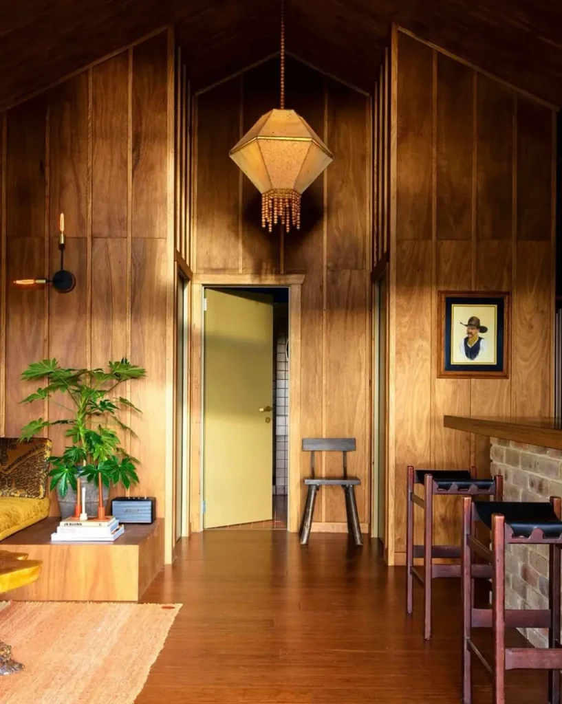 A room showcasing 70s interior design styles with floor-to-ceiling wood paneling, a vaulted ceiling, and a brick bar.