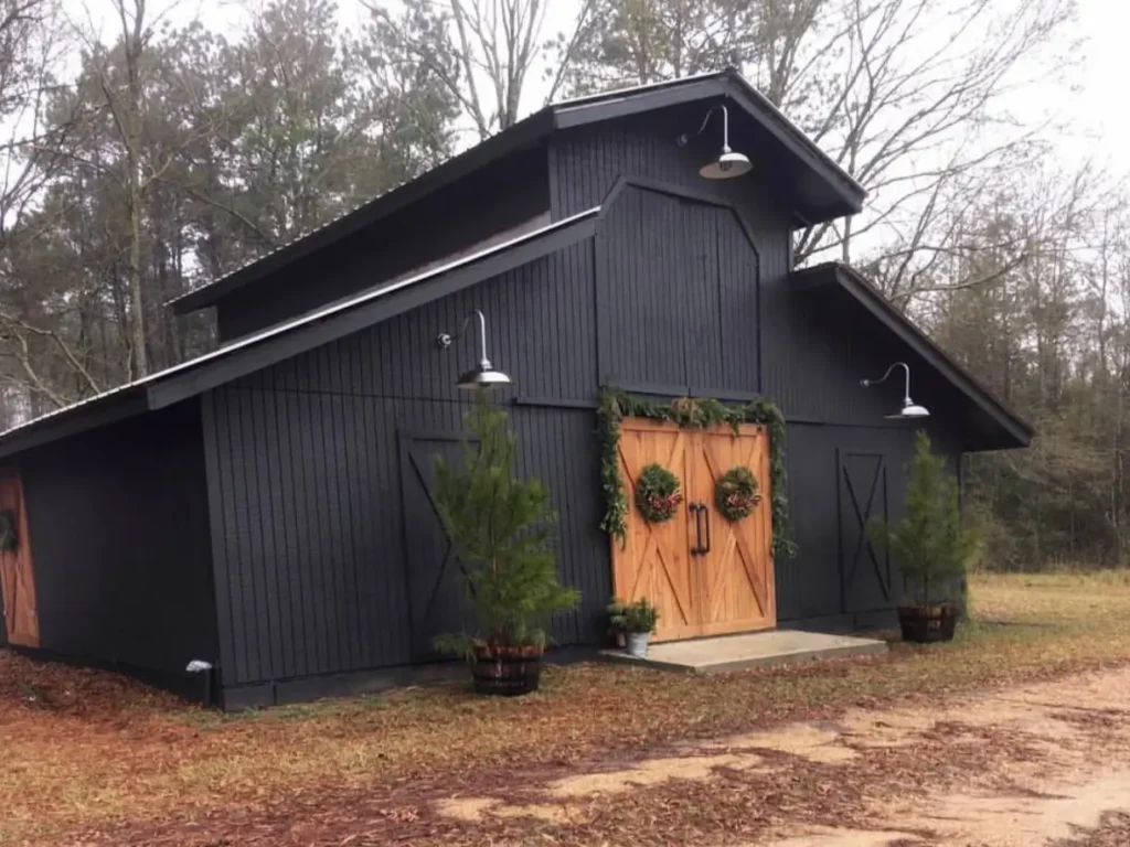 A black barn-style farmhouse with a monitor roof, natural wood cross-brace doors, and gooseneck lighting.