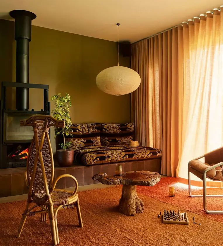 A 70s-style lounge with olive walls, an orange shag rug, a rattan chair, and a built-in sofa.