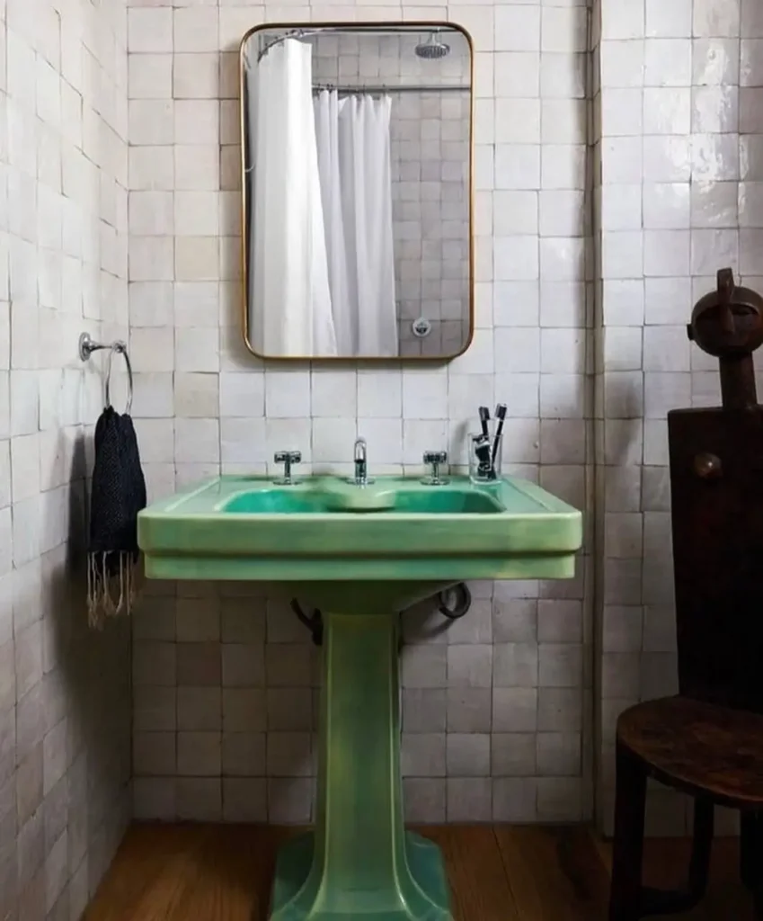 A modern 70s bathroom centered around a vintage avocado green pedestal sink against a white tile wall.
