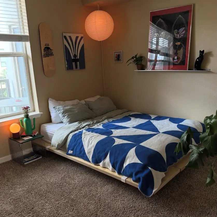 A cozy small apartment bedroom featuring a low-profile bed with a bold blue and white quilt and personal items used as decor.