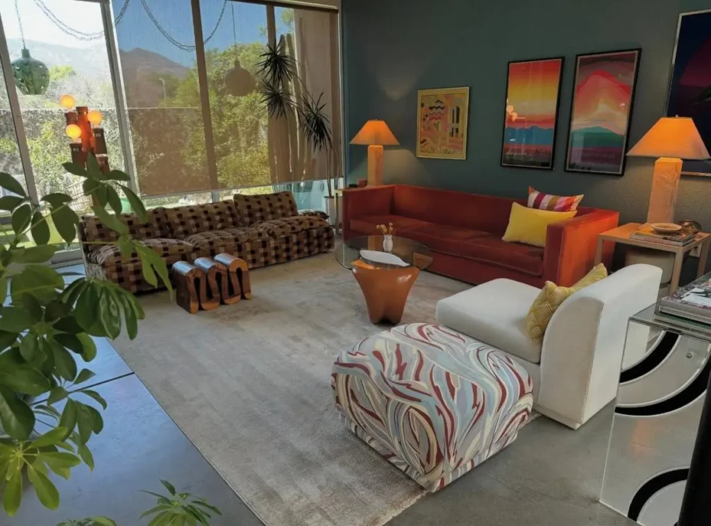 An eclectic 70s living room with a rust-orange sofa, a patterned loveseat, and teal walls.