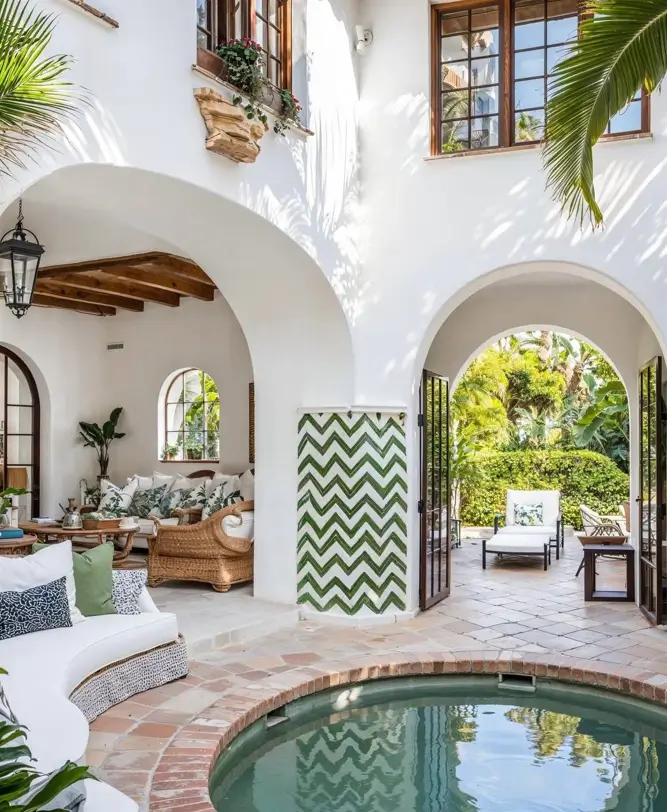 A white stucco Mediterranean courtyard with archways, a round plunge pool, and a green chevron tile accent.