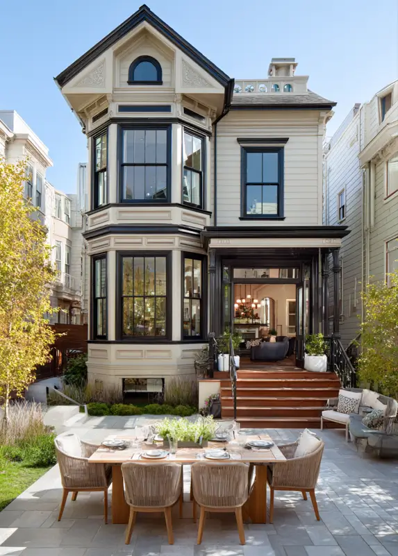 A beige modern Victorian house with black trim and an open front entry flowing onto a stone patio.