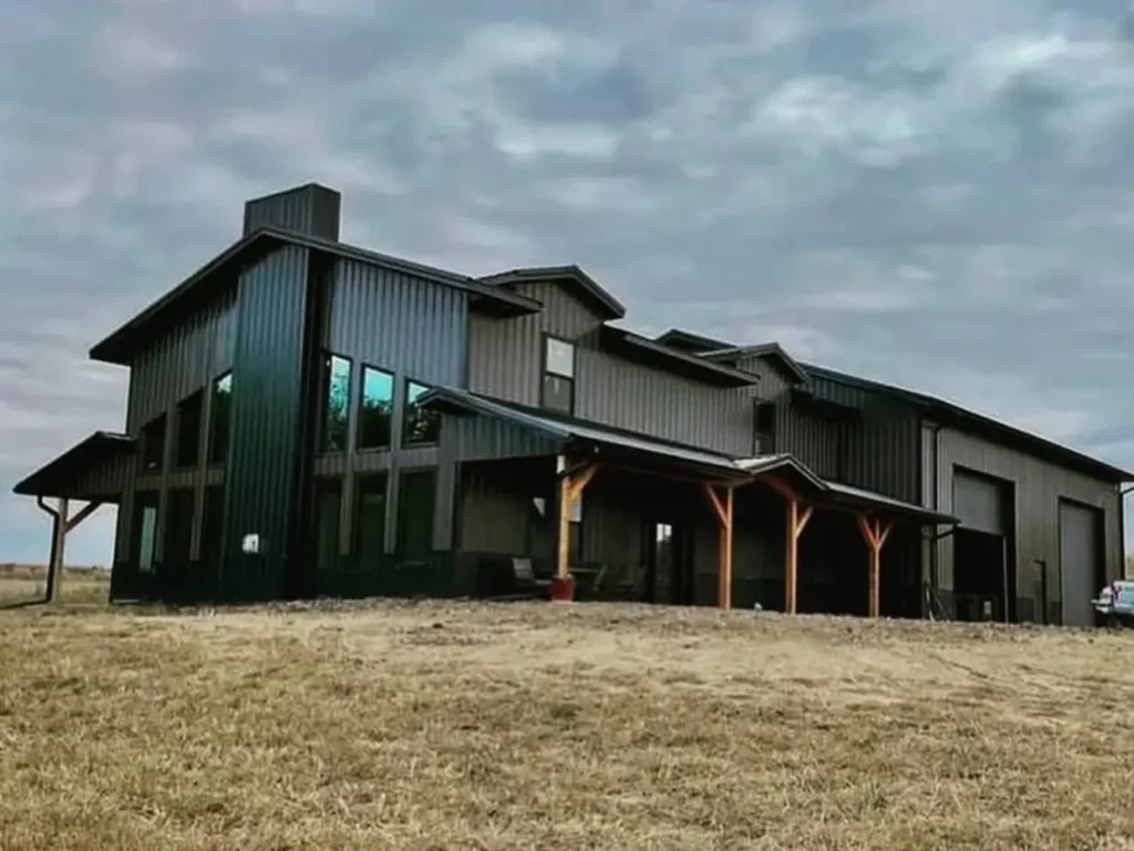 A sprawling black barndominium-style farmhouse with a heavy timber porch under a cloudy sky.