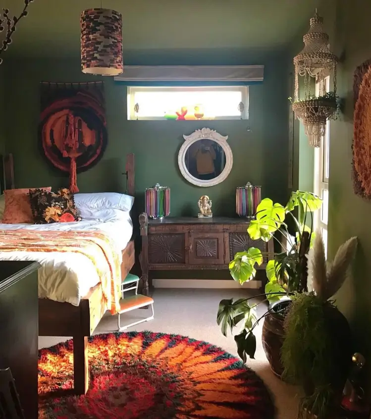 A bohemian bedroom with 70s interior decor, featuring deep green walls, a sunburst shag rug, and woven wall hangings.
