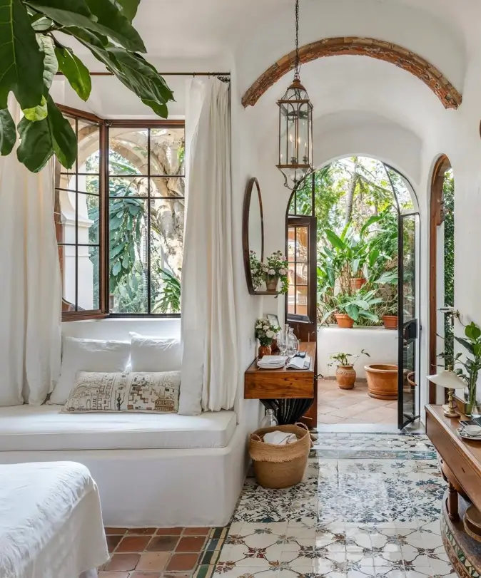 Mediterranean interior with patterned floor tiles, an arched doorway, and white built-in seating opening to a garden.