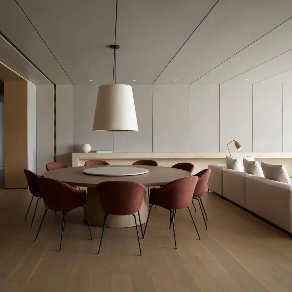 Minimalist dining room with a large round wood table, rust-colored chairs, and an oversized white drum pendant light.