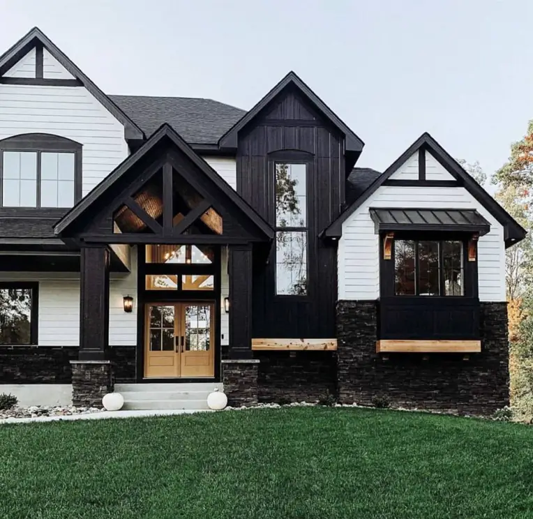 A modern farmhouse with a high-contrast exterior of white siding, bold black accents, and a dark stone base.
