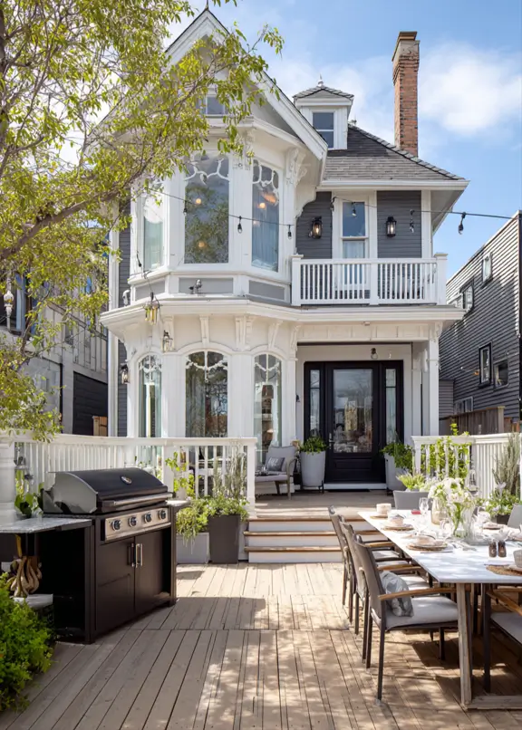 The back of a gray and white modern Victorian style house with a large wooden deck for outdoor dining.