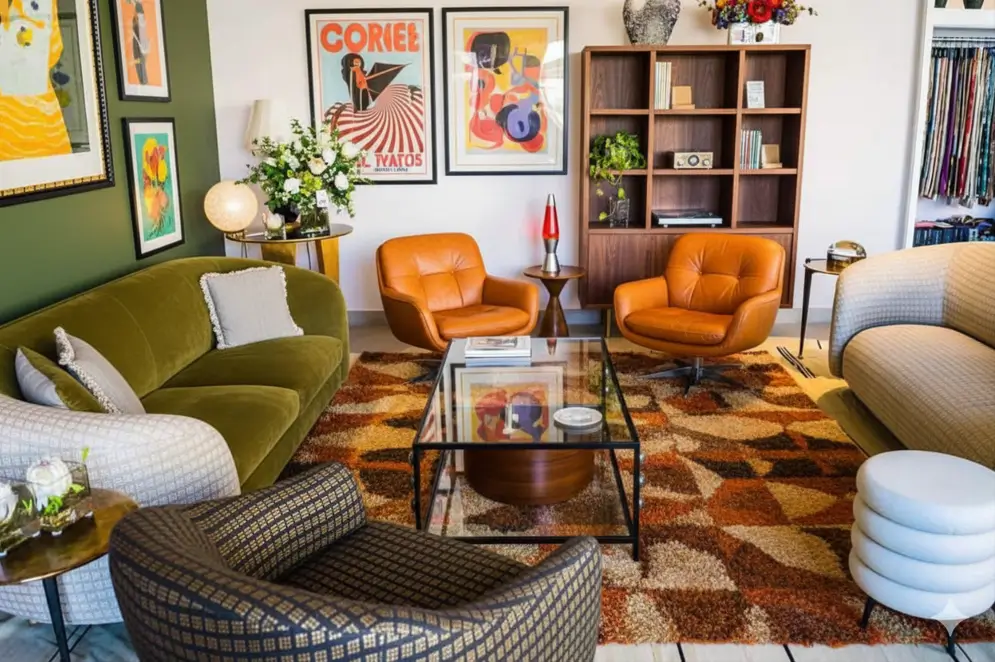 A 70s living room with an olive sofa, orange leather chairs, and a bold geometric shag rug.