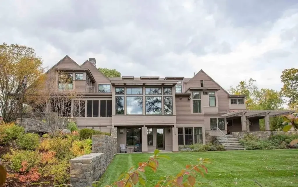 A modern Victorian style home by Eck MacNeely Architects with a green roof and large glass walls, integrated into a hillside with stepped stone retaining walls.
