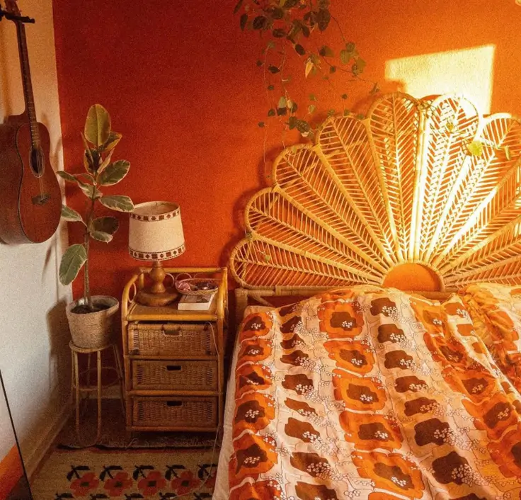 A boho 70s bedroom decor idea with a large rattan peacock headboard against an orange wall.