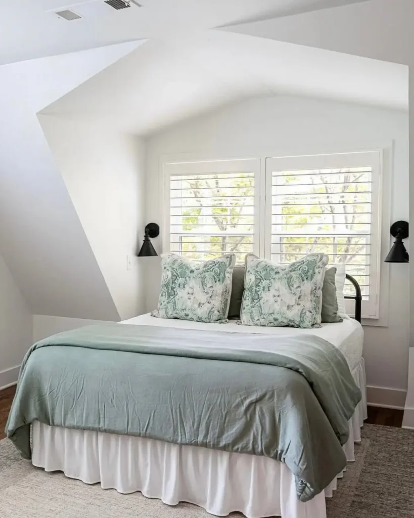 A bright, finished attic bedroom created by a dormer addition, featuring a neatly made bed under a window with white shutters.