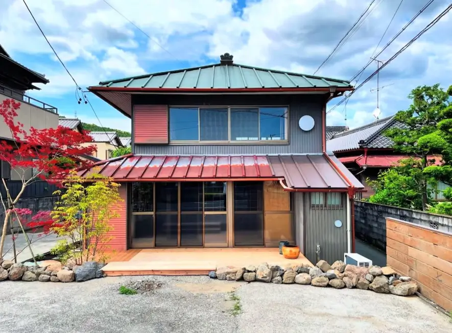 A Japanese style house with a green tiled roof, grey siding, and a light wood deck.