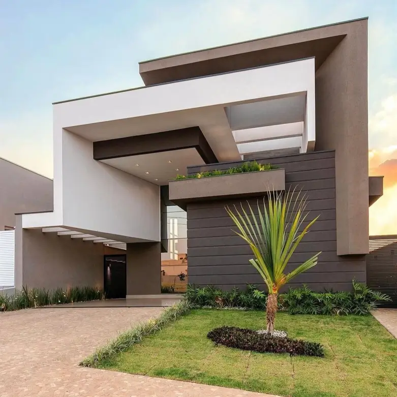 A modern minimalist house with interlocking white and grey geometric shapes and a landscaped front yard at dusk.