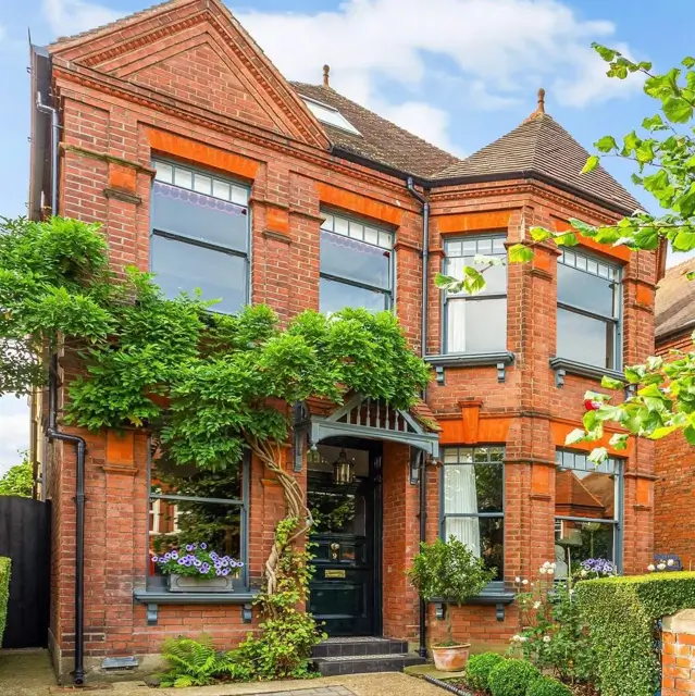 A classic red brick modern Victorian house with dark green trim and a lush vine climbing the facade.