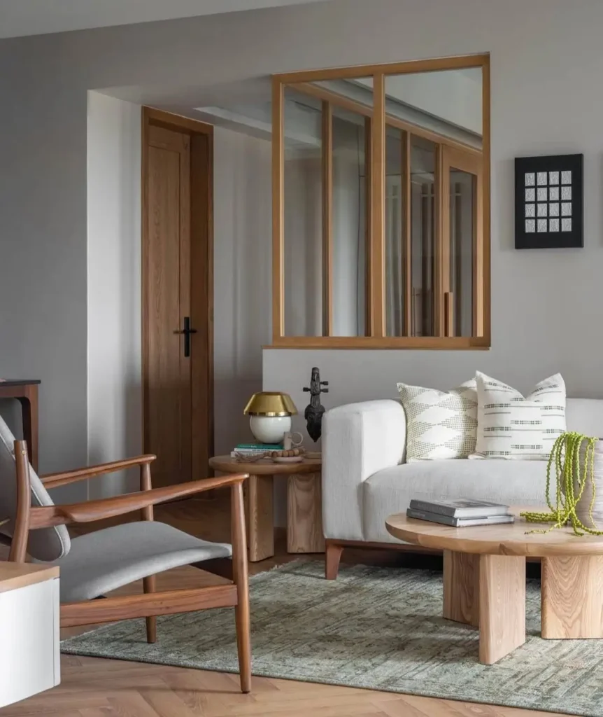 A modern neutral living room featuring a white sofa, a wooden armchair with grey cushions, and a light wood coffee table.