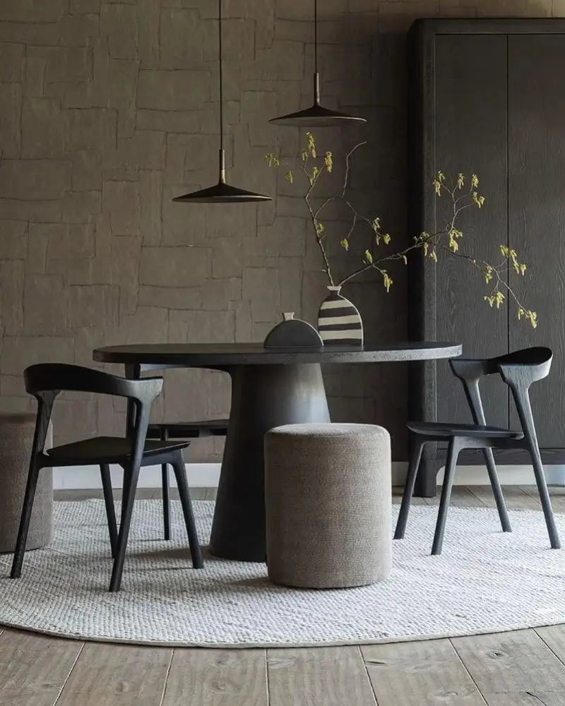 An elegant modern dining room with a dark round table, minimalist black chairs, and a woven rug against a textured wall.