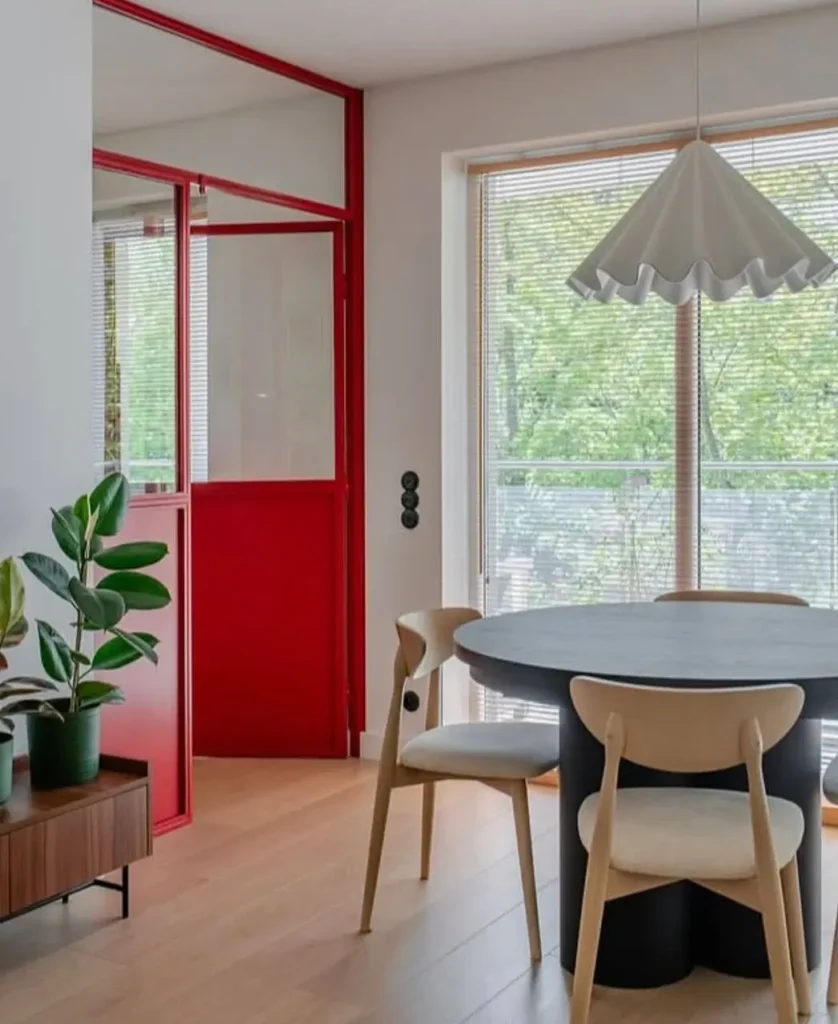 Minimalist dining room by Projektive Architekci with a bold red interior door and a black table.