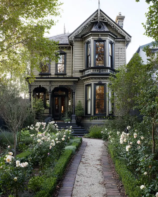 A modern Victorian home in olive green, viewed from a gravel path lined with white roses.